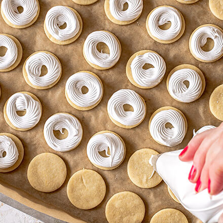 Blog Beitrag Weihnachtsplätzchen Step2 Mithilfe eines Spritzbeutels den Eisschnee auf die fertig gebackenen Plätzen in Kreisen spritzen.