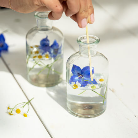 Einfache Tischdeko für den Frühsommer - Step 4: Blüten arrangieren Eine Hand ordnet den Rittersporn im Wasser mit einem Holzstab an.