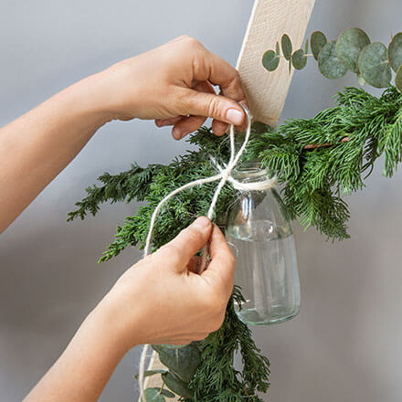 Blog Beitrag Alternativ Weihnachtsbaum Step7 Es werden kleine Milchgläschen mit einer weißen Schnurr an der Girlande befestigt.
