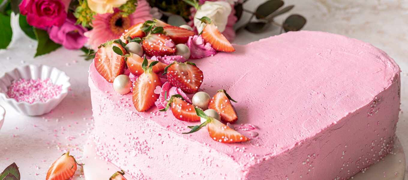 Herztorte backen - Rezeptidee mit Erdbeeren und ohne Herzform rosa Torte in Herzform, dekoriert mit Erdbeeren