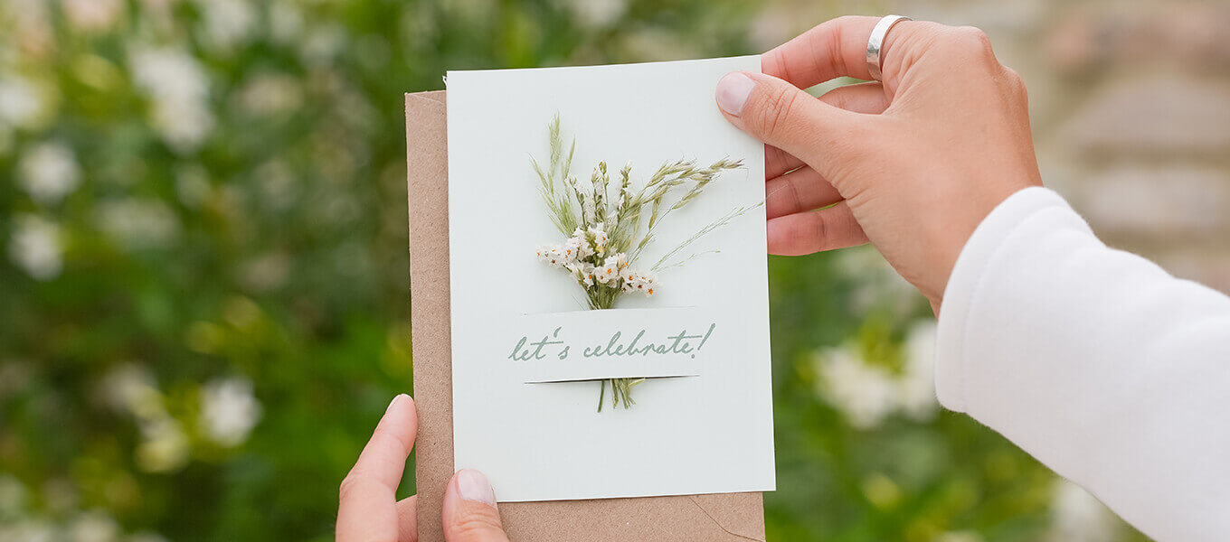 Hochzeitseinladung mit zwei Schlitzen, in die ein Mini-Trockenblumenstrauß gesteckt wurde