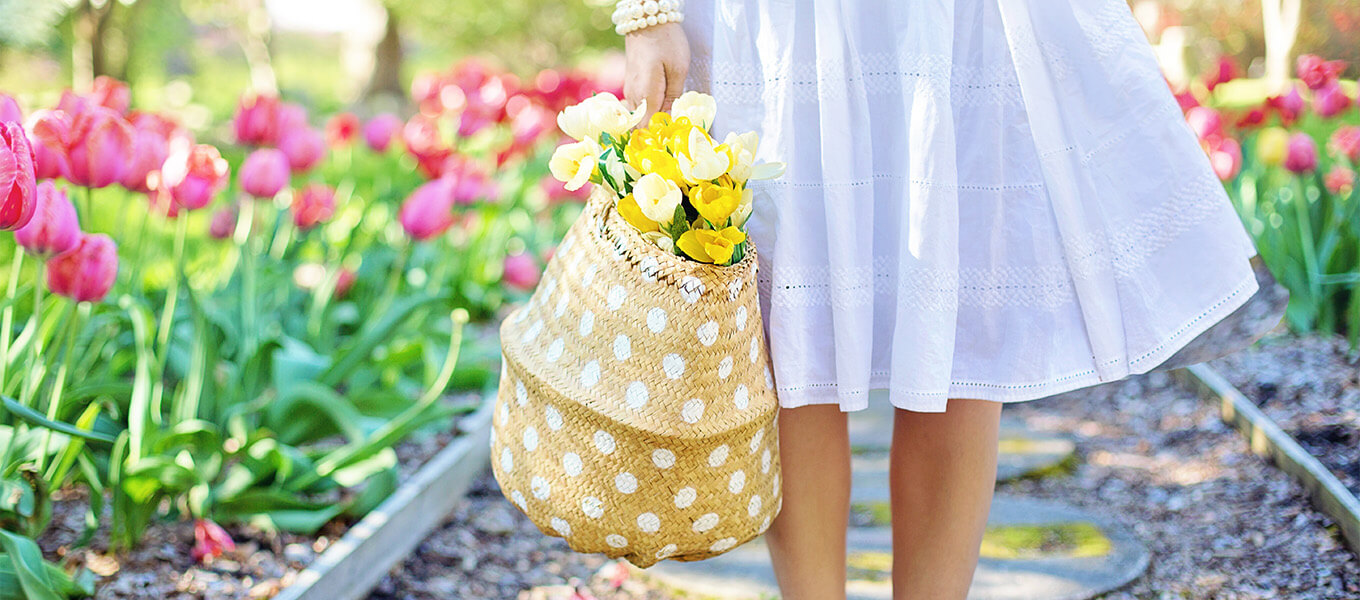 Garten im Frühling - Saisonale Gartentipps Ein Garten im Frühling. Eine Frau steht mit einem Korb, mit Tulpen drinnen im Garten.