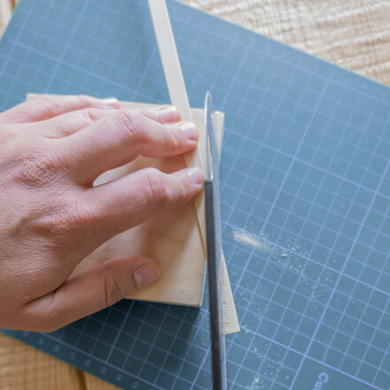 Ein Bambusstab wird mit Hilfe einer  Handsäge auf einer Schneidematte schräg zugeschnitten.