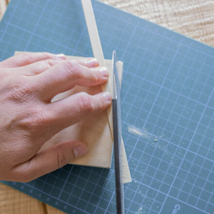 Flower-Bag-Upcycling-Idee zur Vase: Step 6 Ein Bambusstab wird mit Hilfe einer Handsäge auf einer Schneidematte schräg zugeschnitten.