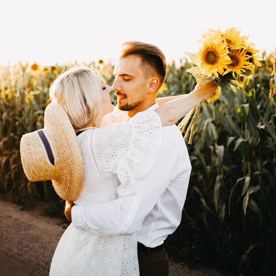 Pärchen vorm Sonnenblumenfeld Ein Pärchen umarmt sich vor einem Sonnenblumenfeld. Die Frau hat ein paar Sonnenblumen in der Hand.