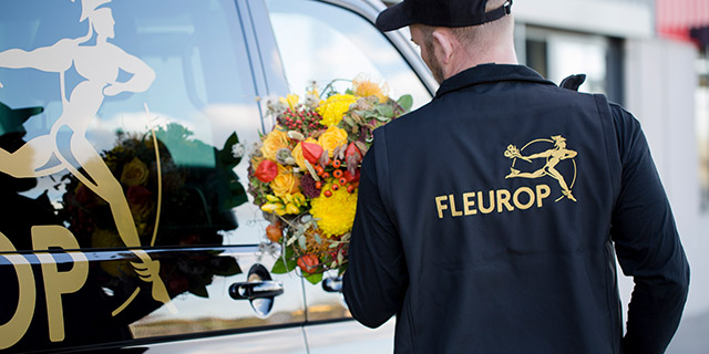 Mann mit Blumenstrauß vor Auto mit Fleurop Logo