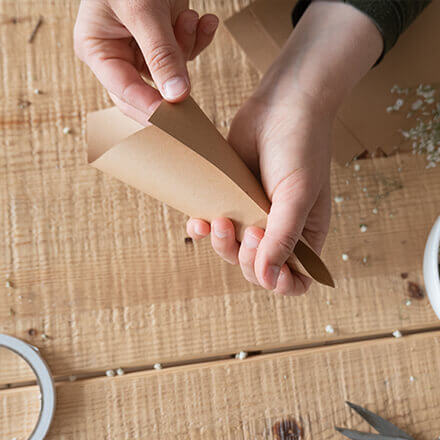 Nachhaltiges Konfetti aus Blumen: Step 3 Zwei Hände falten eine Eistüte aus braunem Papier