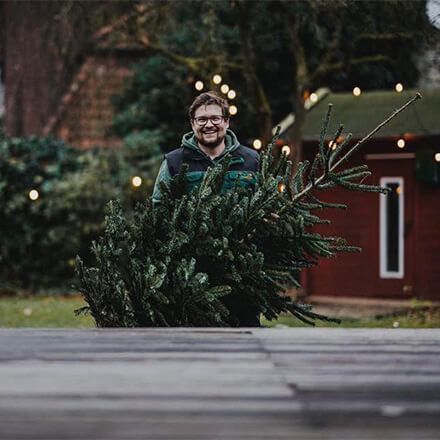 Ein Mann trägt draußen einen Weihnachtsbaum.