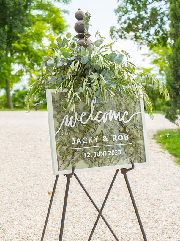 Willkommenschild für eine Hochzeit, bestehend aus einem großen Bilderrahmen, welcher mit Eukalyptus befüllt und dekoriert ist und auf der eine Aufschrift steht