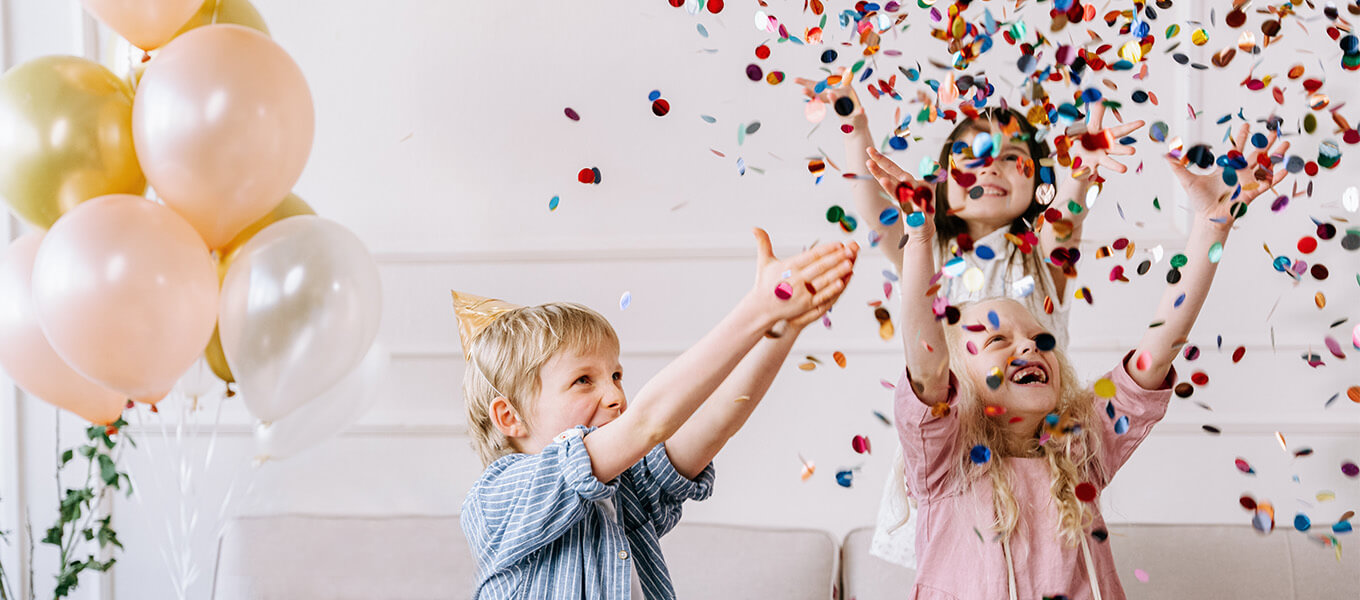Geburtstag Ideen Drei Kinder, die im Wohnzimmer Konfetti auf einer Geburtstagsparty in die Luft werfen