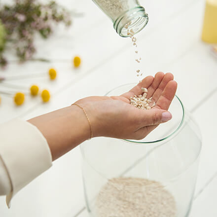 Dekoidee: Windlicht für den Sommertisch - Step 1: Glas mit Dekogranulat befüllen Dekogranulat wird auf eine Hand geschüttet. Unter der Hand befindet sich ein Windlicht, in dem sich schon etwas Granulat befindet.