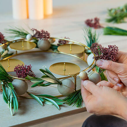 Blog Beitrag Adventskranz Step4 Es werden verschiedene grüne Zweige als Dekoraktion in die Löcher der Kugeln gesteckt.