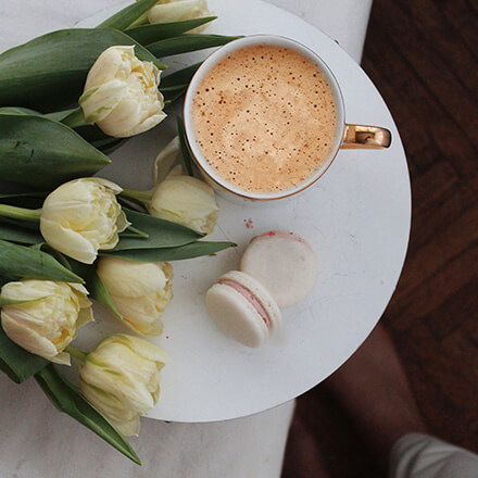 Draufsicht auf Kaffeebecher, links daneben liegen weiße Tulpen