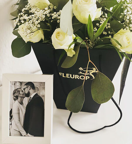 Bilderrahmen mit einem Brautpaar steht vor einem weißen Blumenstrauß