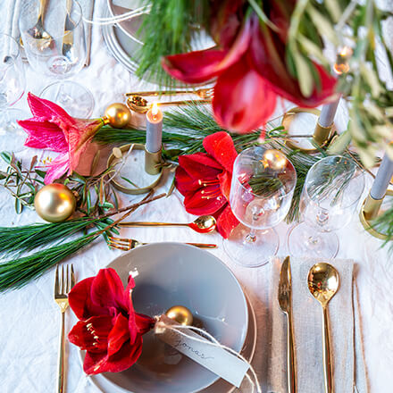Tischdekoration: Eine rote Amaryllisblüte in eine Weihnachtskugel gesteckt und mit einem Namensschild dran.