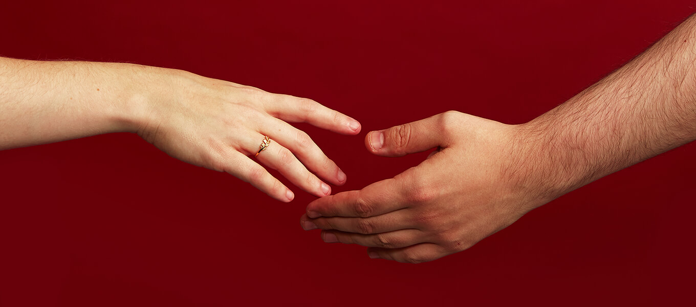 Valentinstag: Sprüche und Gedichte zum Verlieben zwei Hände die nach einander greifen vor rotem Hintergrund