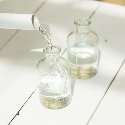 Einfache Tischdeko für den Frühsommer - Step 1: Flaschen mit Wasser befüllen In zwei kleine Ginflaschen wird etwas Wasser mit Hilfe einer Gießkanne gefüllt.
