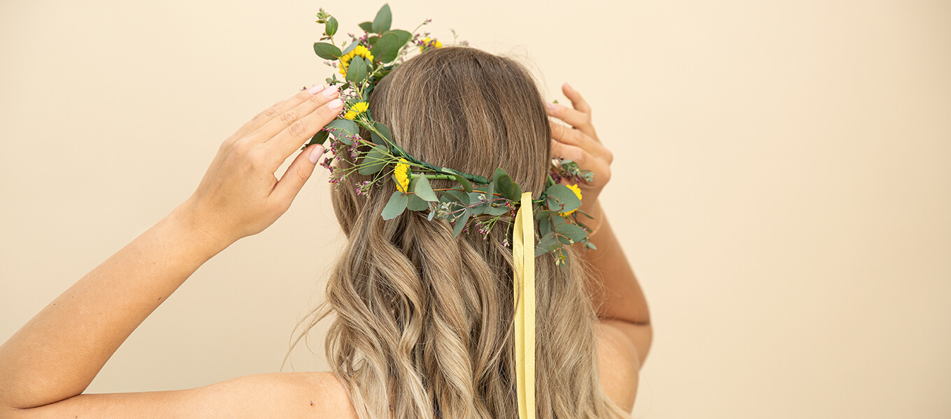 DIY: Haarkranz selbst basteln Person mit brünett-lockigen Haaren hält einen minimalistischen Haarkranz in Grün-Gelb mit beiden Händen auf ihrem Kopf fest.