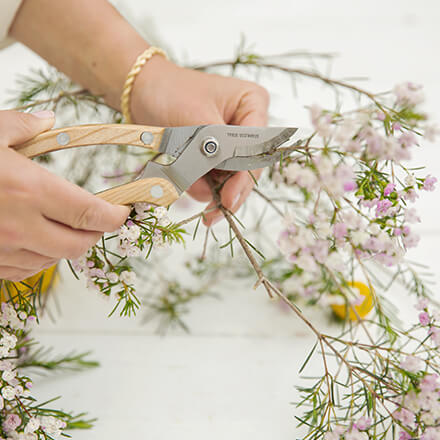 Dekoidee: Windlicht für den Sommertisch - Step 3: Blumen zurechtschneiden Zwei Hände schneiden mit Hilfe einer Floristenschere Waxflower Zuschnitte zu.