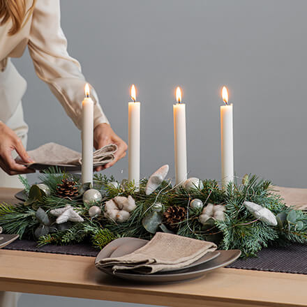 Blog Beitrag Adventskranz - länglicher Adventskranz Ein länglicher Adventskranz mit vier Stabkerzen und klassischer Dekoration wie Tannenzweige, Kugeln und Baumwolle.