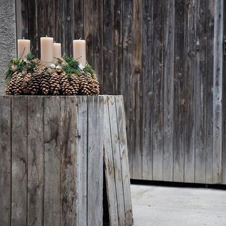 Blog Beitrag Adventskranz - Adventskranz aus Naturmaterialien Ein Adventskranz aus Kiefernzapfen steht in einer Holzscheune.