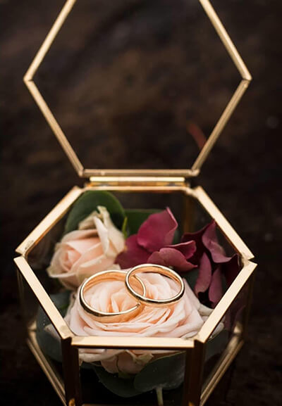 Zwei Eheringe in einer Glasschatulle mit pfirsichfarbenen Rosen