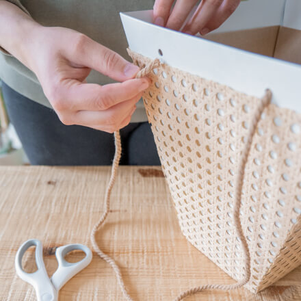 Flower-Bag-Upcycling-Idee zur Geschenkbox: Step 6 Der Flower-Bag wird bei einer Upcycling-Idee zu einer Geschenkbox mit Wiener Geflecht die Henkel in Form von Baumwollschnur in Naturfarben wieder angebracht.