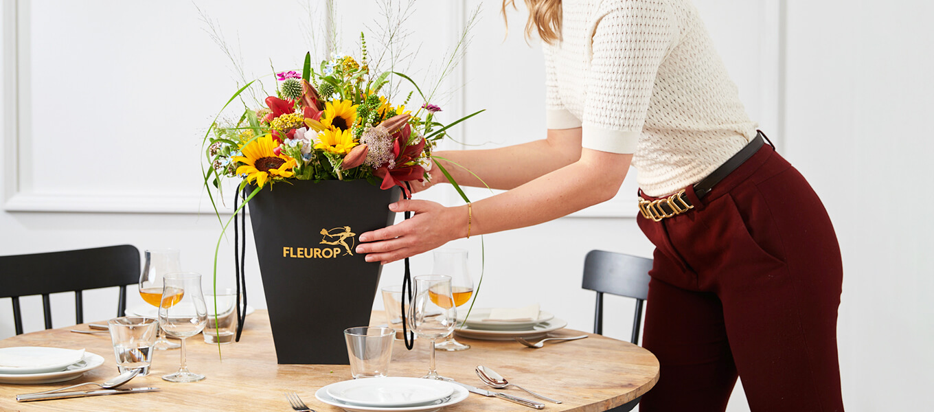Frau stellt einen Blumenstrauß in einer Flower-Bag auf einen gedeckten Tisch