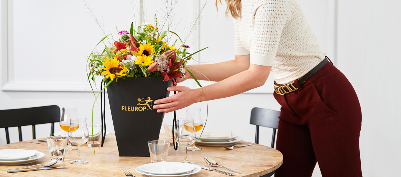 Ideen Flower-Bag Frau stellt einen Blumenstrauß in einer Flower-Bag auf einen gedeckten Tisch