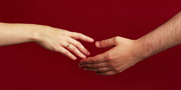 zwei Hände die nach einander greifen vor rotem Hintergrund